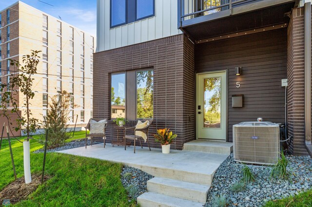 view of exterior entry featuring a balcony, a patio, central AC unit, and a yard