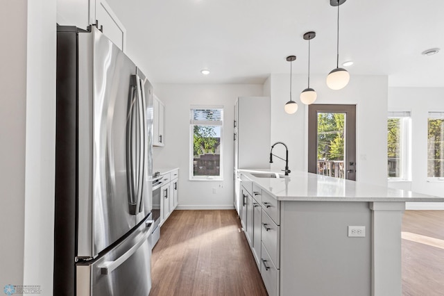 kitchen featuring wood finished floors, baseboards, a sink, hanging light fixtures, and stainless steel appliances