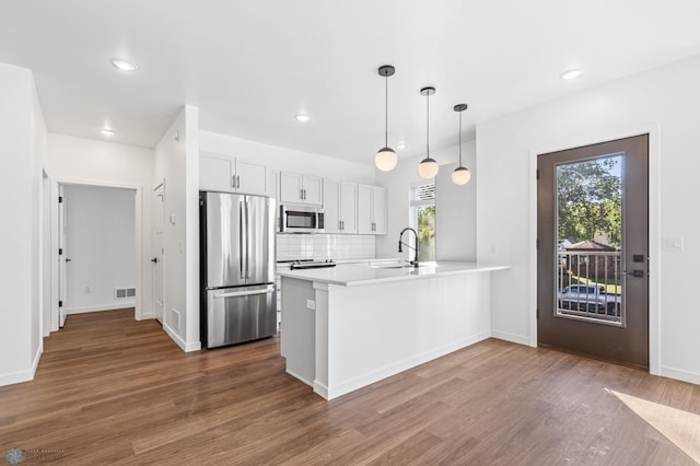 kitchen with appliances with stainless steel finishes, a sink, a peninsula, visible vents, and dark wood-style floors