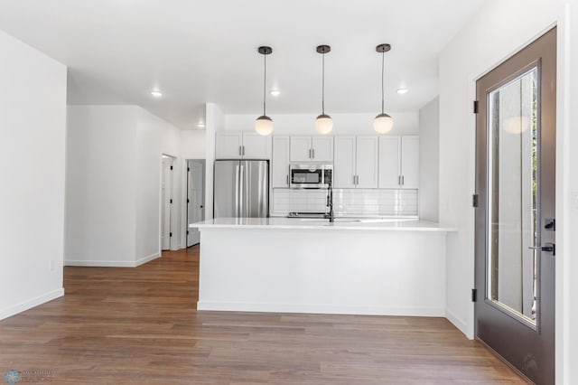 kitchen featuring a peninsula, wood finished floors, light countertops, appliances with stainless steel finishes, and backsplash