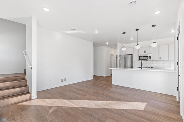 kitchen with appliances with stainless steel finishes, recessed lighting, a peninsula, decorative backsplash, and wood finished floors