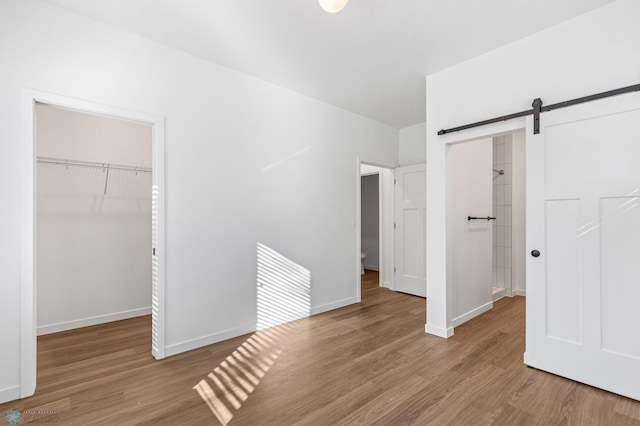 unfurnished bedroom with a closet, wood finished floors, baseboards, a barn door, and a spacious closet