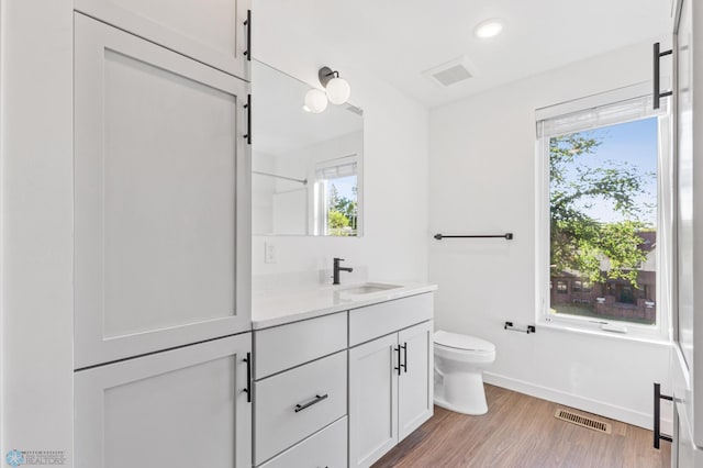bathroom with visible vents, vanity, wood finished floors, toilet, and baseboards