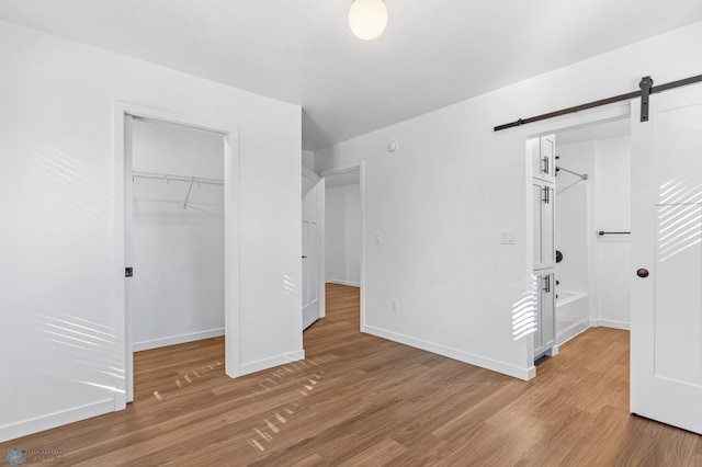 unfurnished bedroom featuring a walk in closet, a barn door, baseboards, a closet, and light wood finished floors