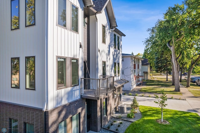 view of property exterior featuring a balcony, cooling unit, brick siding, a shingled roof, and a lawn