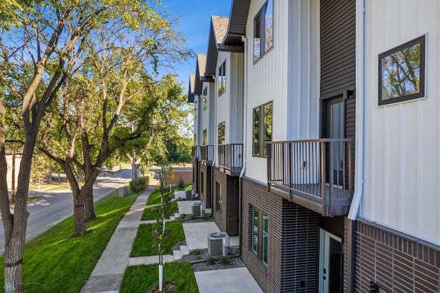 view of side of property featuring board and batten siding, central AC, and a balcony