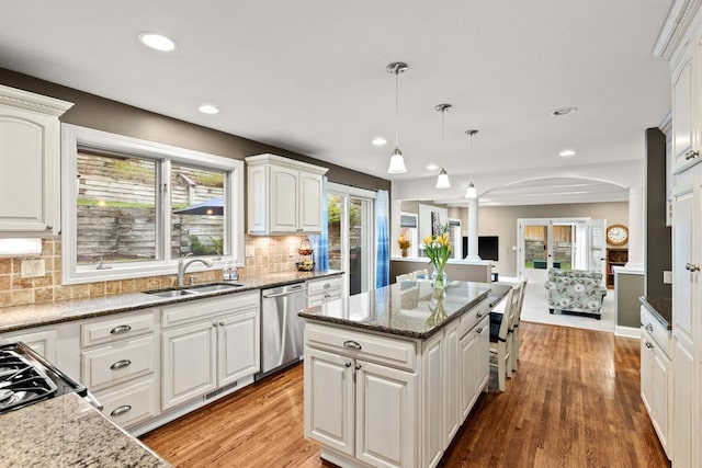 kitchen featuring backsplash, stainless steel dishwasher, sink, white cabinets, and hanging light fixtures