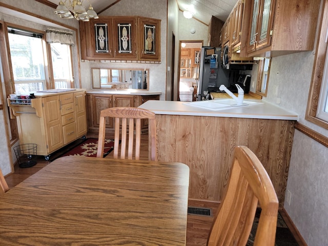 kitchen featuring vaulted ceiling, kitchen peninsula, an inviting chandelier, and dark wood-type flooring