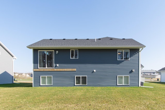 rear view of house with roof with shingles and a yard