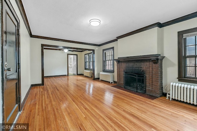 unfurnished living room with radiator heating unit, a brick fireplace, a textured ceiling, and light hardwood / wood-style flooring