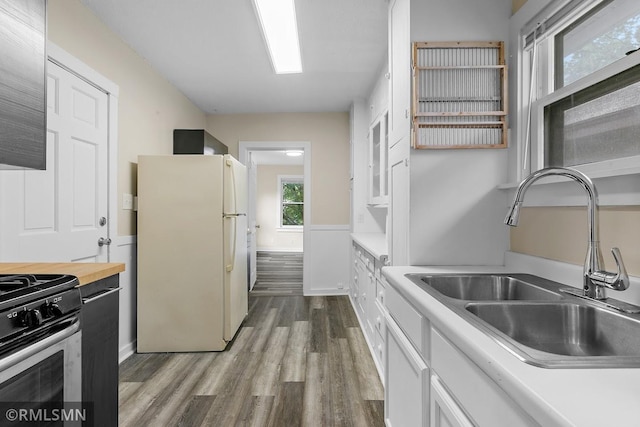 kitchen with white refrigerator, hardwood / wood-style flooring, sink, white cabinetry, and black gas range