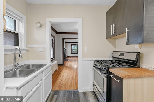 kitchen featuring ornamental molding, dark brown cabinets, stainless steel gas stove, dark hardwood / wood-style floors, and sink