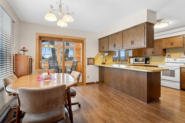 kitchen with light wood-type flooring, kitchen peninsula, a notable chandelier, pendant lighting, and white appliances