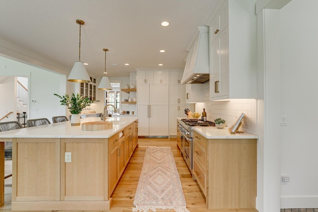 kitchen featuring a breakfast bar, custom range hood, a large island with sink, range with two ovens, and white cabinets