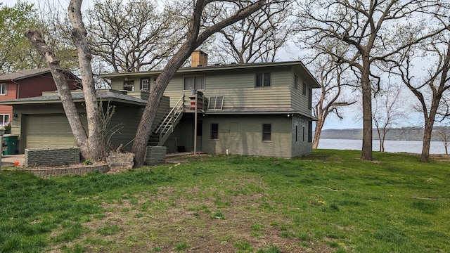 rear view of property featuring an attached garage, a water view, stairs, a lawn, and a chimney