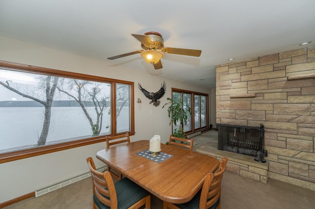 carpeted dining room featuring ceiling fan, baseboard heating, a water view, and a fireplace