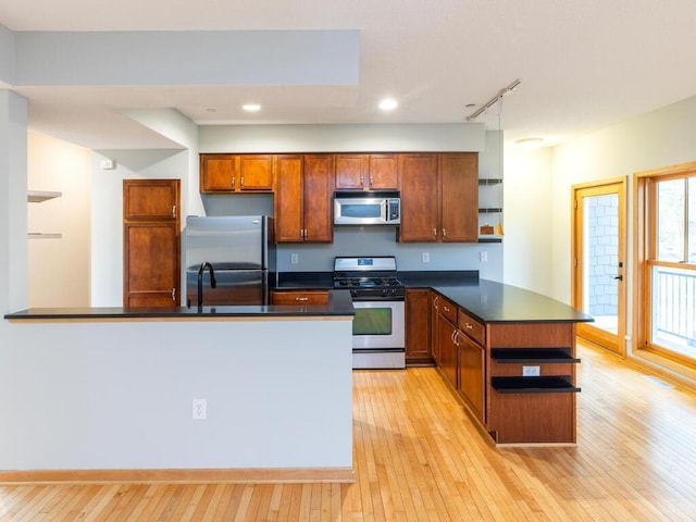 kitchen with stainless steel appliances, rail lighting, kitchen peninsula, and light hardwood / wood-style flooring