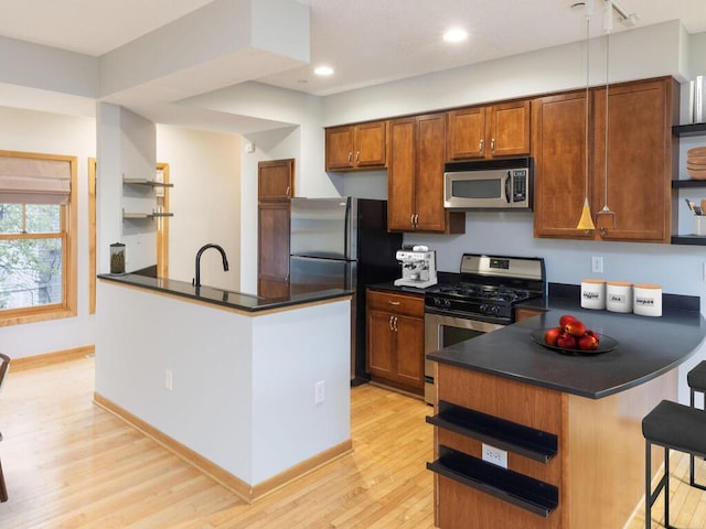 kitchen with sink, a breakfast bar area, kitchen peninsula, stainless steel appliances, and light wood-type flooring