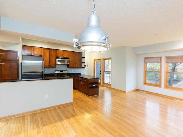 kitchen with a kitchen island, decorative light fixtures, stainless steel appliances, a textured ceiling, and light hardwood / wood-style flooring