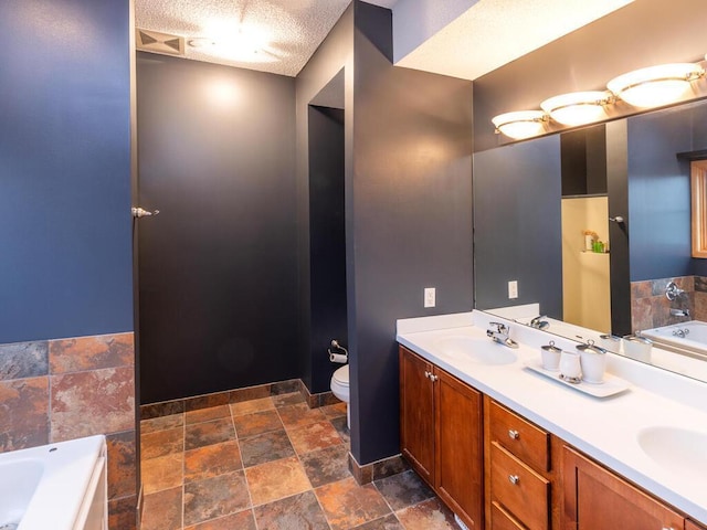 bathroom with vanity, toilet, a bathtub, and a textured ceiling