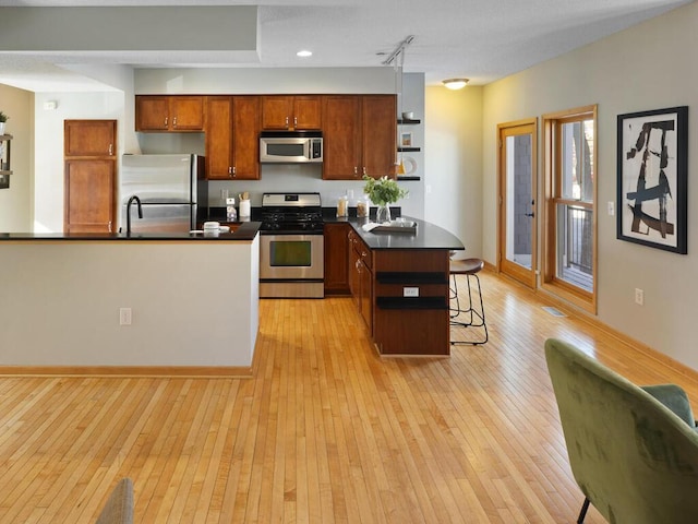 kitchen with appliances with stainless steel finishes, a center island, light hardwood / wood-style floors, track lighting, and a breakfast bar area