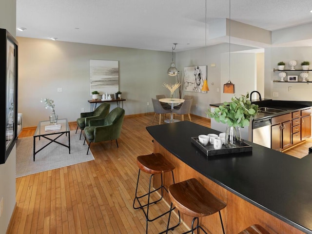 interior space featuring light hardwood / wood-style floors, sink, stainless steel dishwasher, a breakfast bar area, and pendant lighting