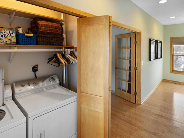 clothes washing area with washing machine and clothes dryer and light wood-type flooring