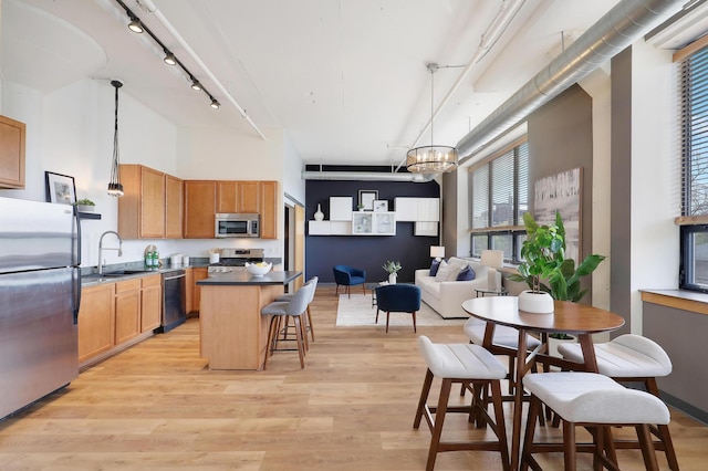 kitchen with sink, stainless steel appliances, light hardwood / wood-style flooring, decorative light fixtures, and a breakfast bar area