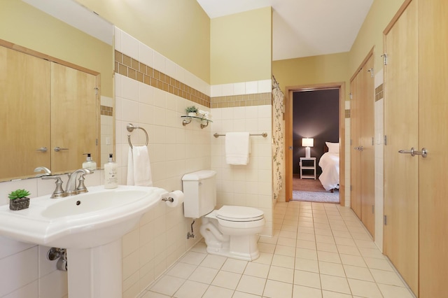 bathroom with toilet, tile patterned floors, tile walls, and sink