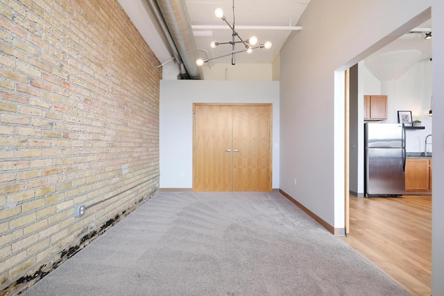 hall with brick wall, light colored carpet, sink, an inviting chandelier, and a high ceiling