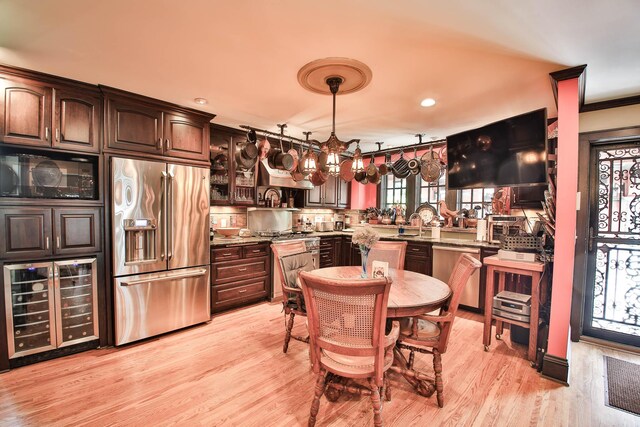 kitchen with pendant lighting, dark brown cabinets, premium appliances, light hardwood / wood-style floors, and beverage cooler