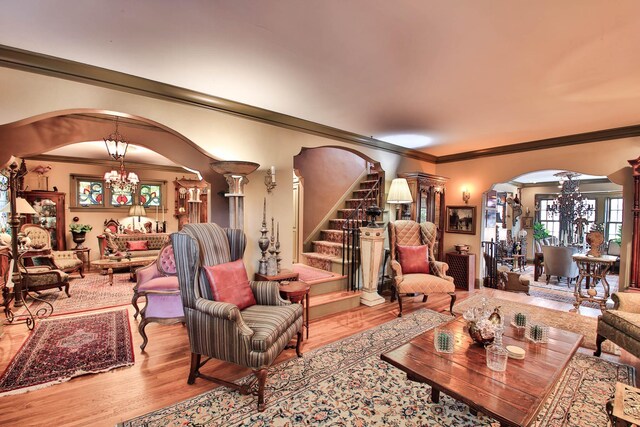 living room featuring ornate columns, ornamental molding, an inviting chandelier, and light hardwood / wood-style floors