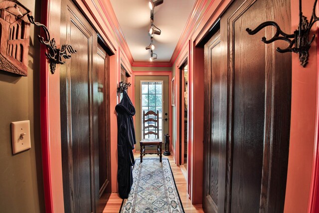 hallway featuring ornamental molding, rail lighting, and light hardwood / wood-style flooring