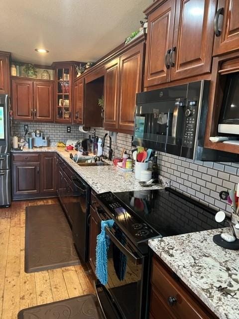 kitchen with backsplash, light stone counters, black appliances, and light hardwood / wood-style floors