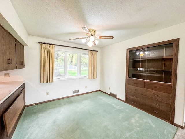 unfurnished dining area featuring light carpet, a textured ceiling, and ceiling fan