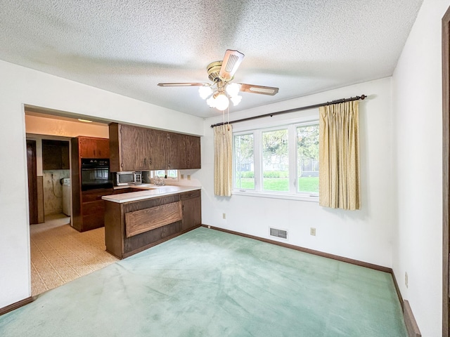 kitchen with oven, ceiling fan, a textured ceiling, dark brown cabinetry, and light colored carpet