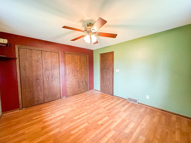 unfurnished bedroom with ceiling fan, multiple closets, a textured ceiling, and hardwood / wood-style floors