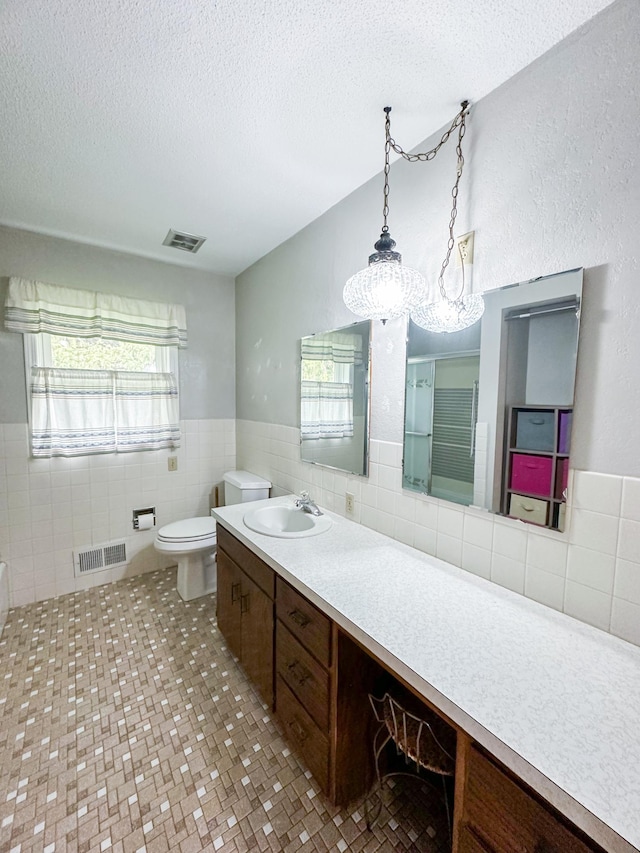 bathroom with a textured ceiling, toilet, tile walls, vanity, and a chandelier