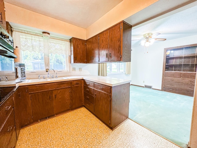 kitchen with sink, kitchen peninsula, light colored carpet, and ceiling fan