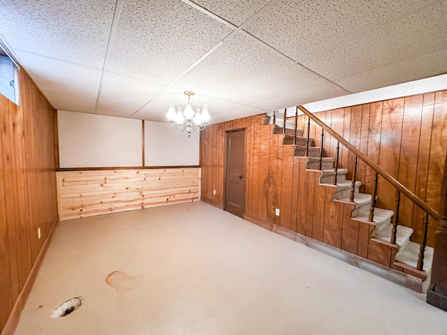 basement featuring an inviting chandelier, a drop ceiling, and wooden walls