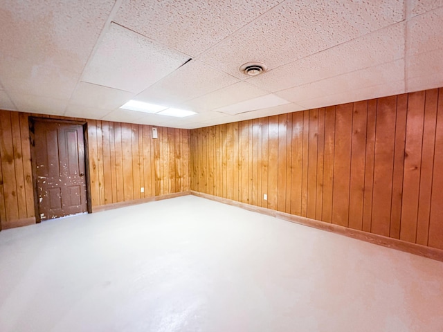 basement featuring a paneled ceiling and wood walls