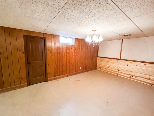 basement with wooden walls, a notable chandelier, a paneled ceiling, and carpet