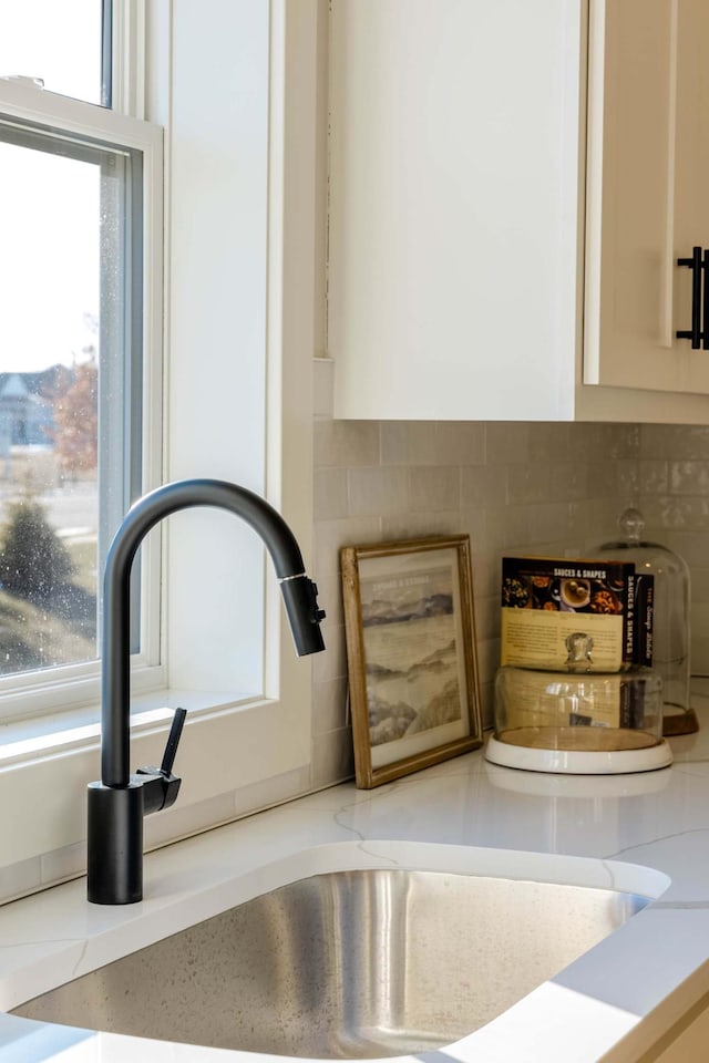 details with backsplash, light stone counters, white cabinetry, and sink