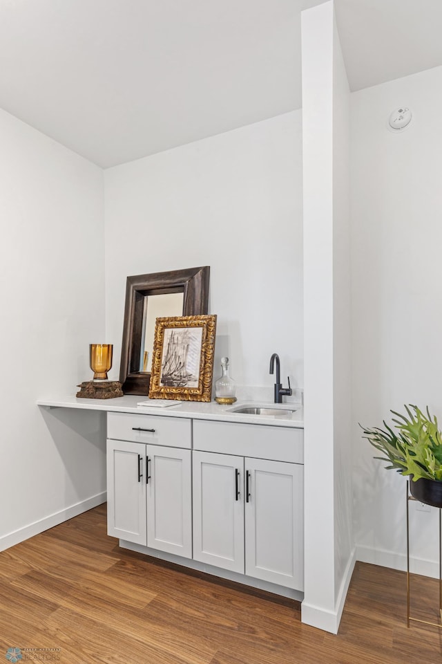 bar featuring baseboards, light wood-style flooring, a sink, and indoor bar