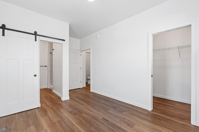 unfurnished bedroom featuring a closet, a barn door, wood finished floors, a walk in closet, and baseboards