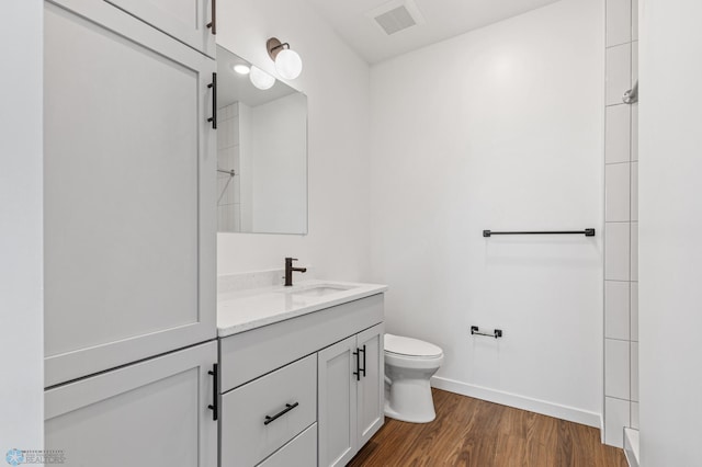 full bath with vanity, toilet, baseboards, visible vents, and wood finished floors