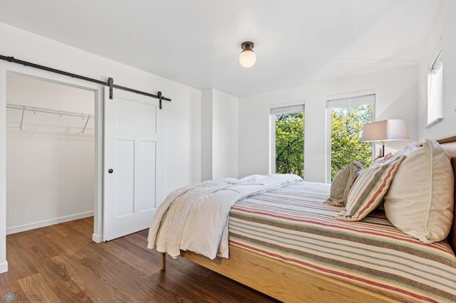 bedroom featuring a closet, baseboards, wood finished floors, a barn door, and a walk in closet