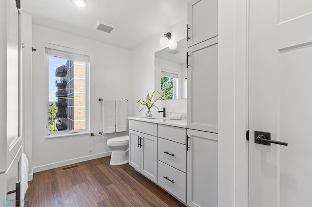 bathroom featuring toilet, vanity, wood finished floors, baseboards, and visible vents