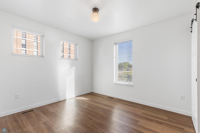 spare room featuring plenty of natural light, visible vents, a barn door, and wood finished floors