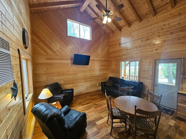 living room with hardwood / wood-style floors, wood walls, high vaulted ceiling, ceiling fan, and beam ceiling